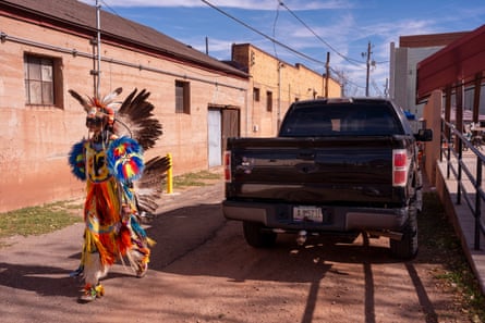 A Native American dancer, dressed in his traditional regalia, walking past a truck on a back road