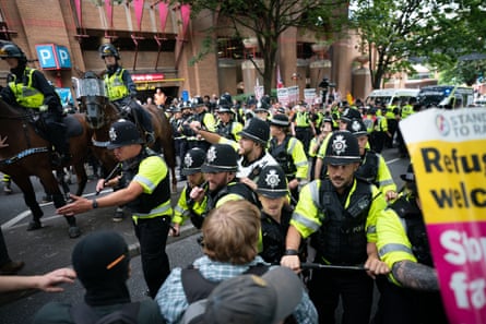 Police officers, some mounted, scuffle with demonstrators by a city centre car park