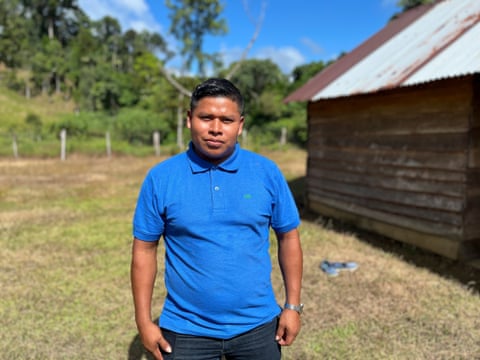 An Indigenous Colombian man stands next to a building in a field