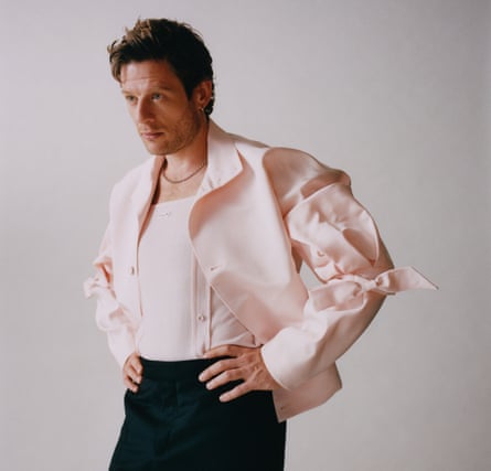 Actor James Norton, hands on hips, in pink shirt and black trousers