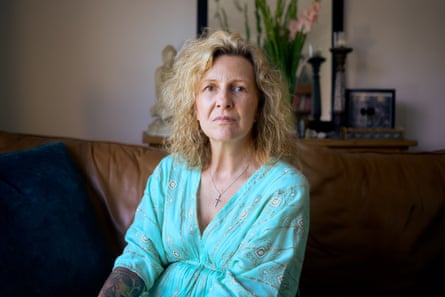 A blonde woman in an aquamarine dress poses solemnly for a portrait in a living room.