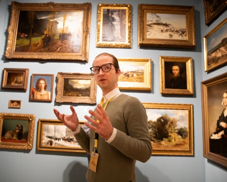 Joseph Langelinck gestures as he talks in front of a wall full of paintings