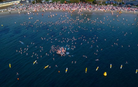 Large aerial of thousands of swimmers plunging into the river.
