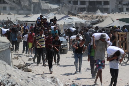 people walk on a road, some with sacks of flour on their backs