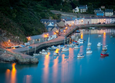 Harbour and sea wall and small boats beautifully lit and houses at dusk