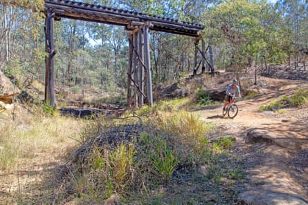 A cyclist riding under an old railway overpass in bushland in the Brisbane Valley Rail Trail