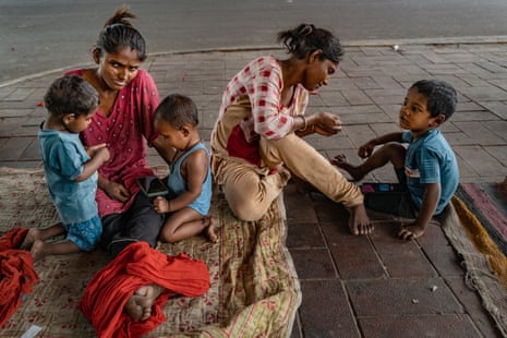 Two women kneel on a blanket interacting with three small children