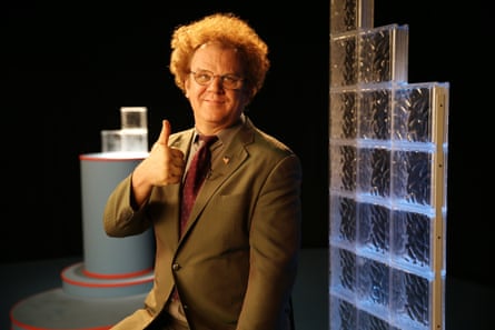 John C Reilly in a studio, wearing a greenish suit and glasses, holding a thumbs up