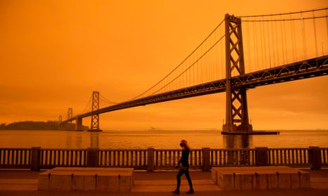 A woman walks under an orange smoke-filled sky in San Francisco.