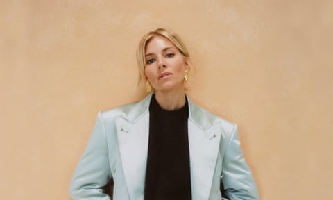Head shot of actor Sienna Miller in turquoise suit against pinky-brown background
