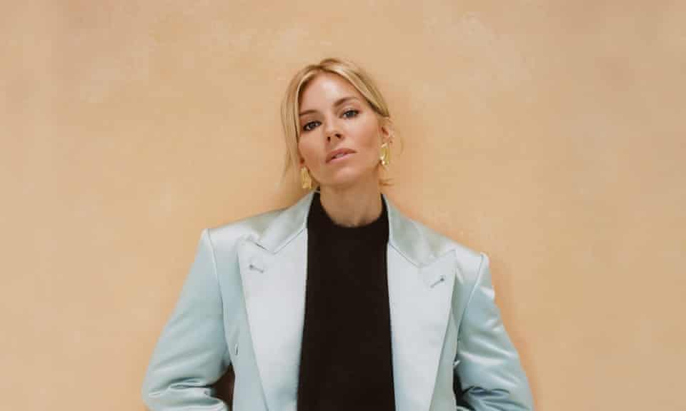 Head shot of actor Sienna Miller in turquoise suit against pinky-brown background