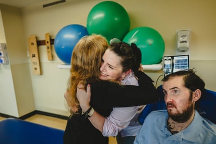 Two woman hugging next to a man