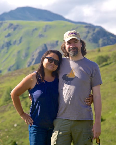 A woman and man posing for a picture, holding each other’s waist. Green hills are behind them.