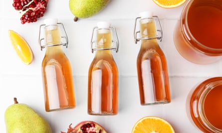 Tasty kombucha and fresh fruits on a white tiled table.