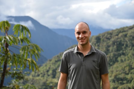 Alexandre Antonelli stands smiling in front of a jungle view with trees, clouds and mountains stretching into the distance.