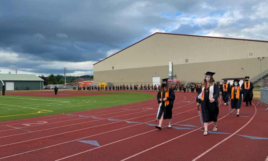 Students wearing graduation gowns walking down a running track