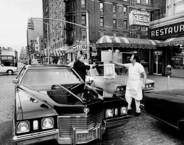 A man hands a bag full of food to a man standing at a car
