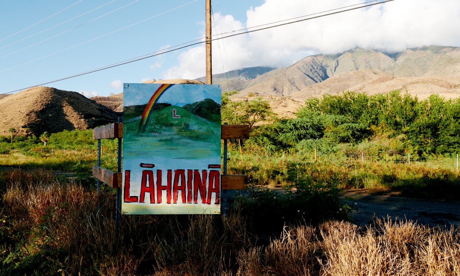 A poster-size, hand-painted sign with Lahaina in red capital letters below a picture of green hills, blue ocean and a rainbow.