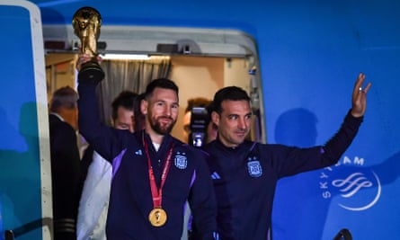 Lionel Messi tient la Coupe du monde, flanqué de l'entraîneur argentin Lionel Scaloni, alors qu'ils descendent de l'avion à Buenos Aires