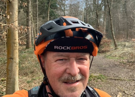 Headshot of David Cross with a black and orange bike helmet with trees in the background.
