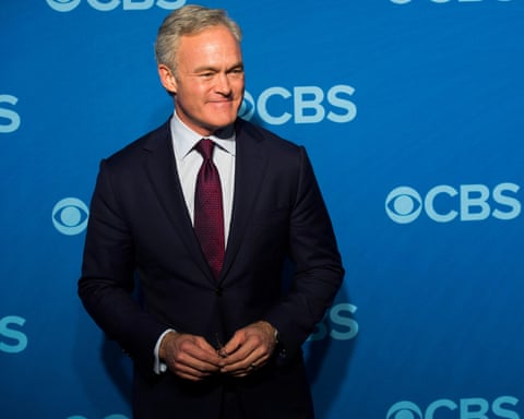 man in a dark suit and red tie stands in front of a blue backdrop with CBS logos
