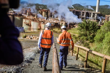 Two men in safety vests walk towards an alumina smelter in Gladstone