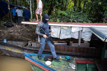 A man in a balaclava steps on to a small boat on a riverbank