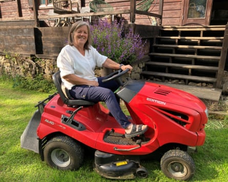 A woman smiles as she sits on an read lawnmower