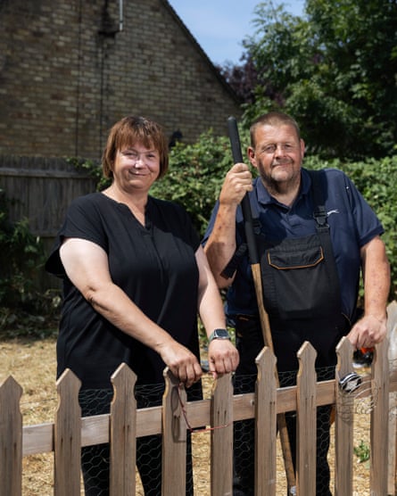 They stand side by side at a picket fence, smiling for the camera. He is holding a hoe in one hand