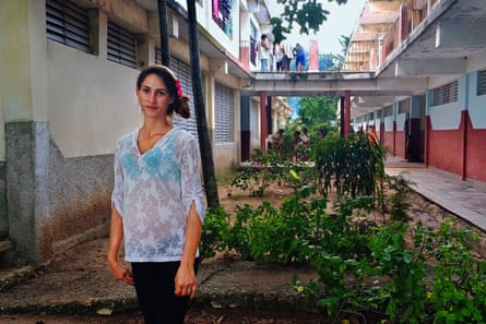 A woman wearing a hairband and white top stands between houses