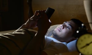 Young man using a smartphone in his bed at night
