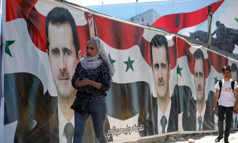People walking past campaign billboards of Bashar al-Assad