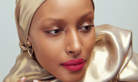 Shahira Yusuf with bright red/pink lips, a gold scarf around her head and shoulders