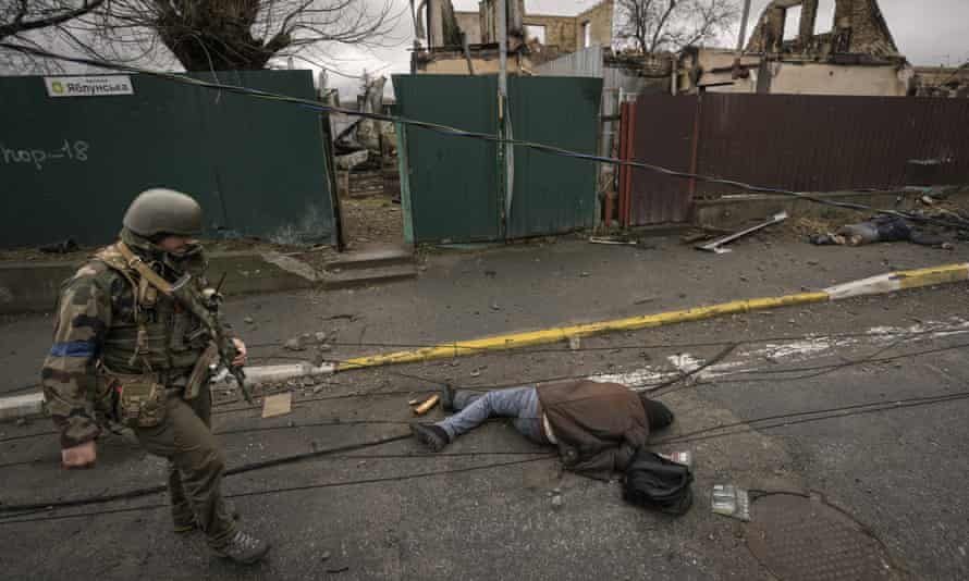 Un militaire ukrainien passe devant un cadavre gisant dans une rue de Bucha
