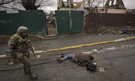 A Ukrainian serviceman walks past a dead body lying on a street of Bucha