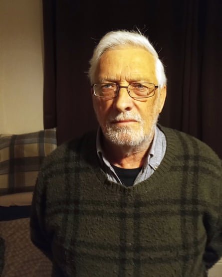 Guy Eyres, 77, from Wales – he has short grey hair and a grey beard, wears a dark green jumper with black checked pattern and spectacles, and looks sternly into the camera