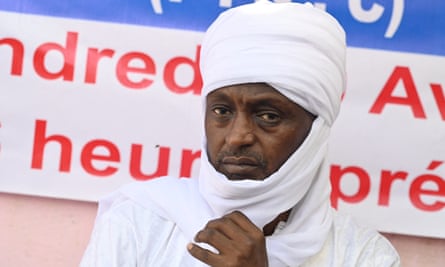 Yaya Dillo, wearing a white kaftan and sitting in front of an election banner
