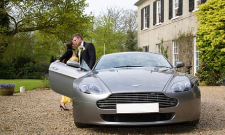 Couple kissing by an Aston Martin outside a country house