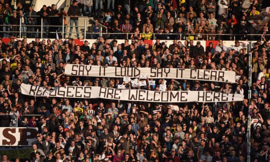 Football fans raise a banner welcoming refugees