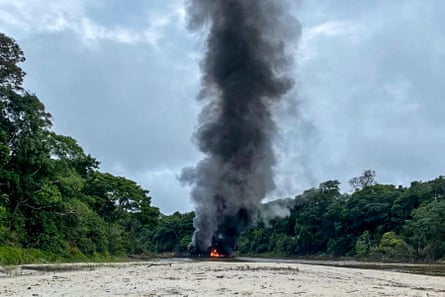 Dredge boat on fire in the Amazon river, with a big black plume of smoke rising against forest trees