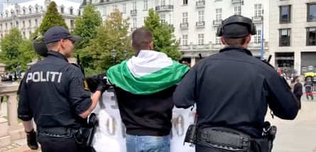 Rear view of man with Palestinian flag with officers each holding one of his arms