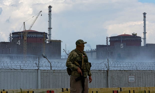 A soldier with a Russian flag on his uniform guards a fence at the Zaporizhzhia nuclear power plant.