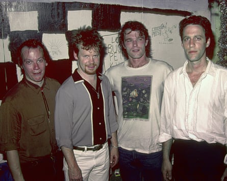 Four men in a band pose for a photo with black and white checkered background