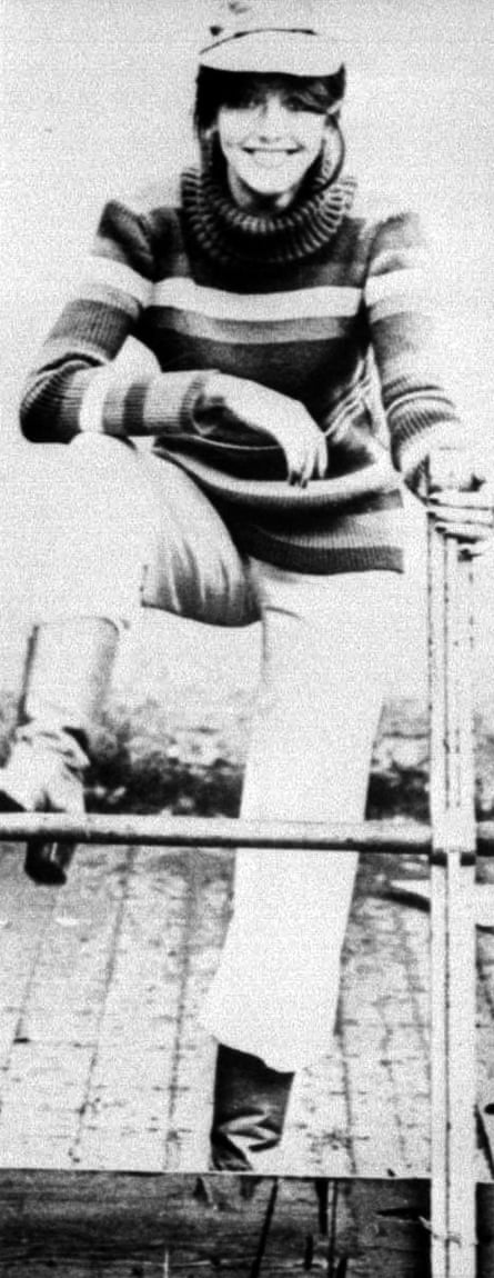 A black and white image of a dark-haired woman wearing a cap, a stripy jumper, light-coloured trousers and boots