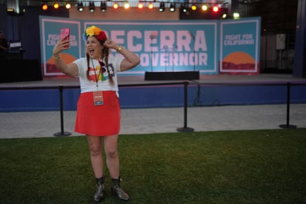 A woman in a rainbow-colored flower headband, a Pride T-shirt and red skirt records herself in front of a Becerra for governor sign.