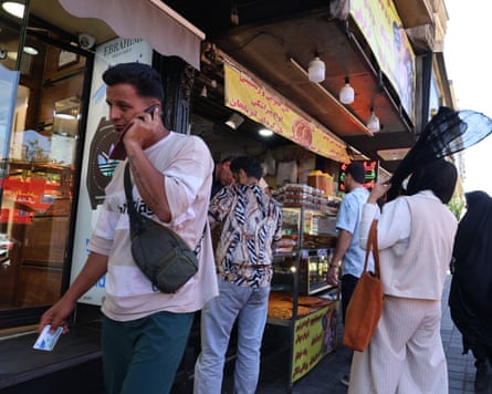 A man speaks on his mobile phone as others stop at a bakery along a street in Tehran