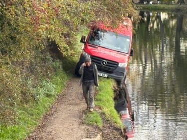 A red Parcelforce van leaning towards the water on a canal towpath