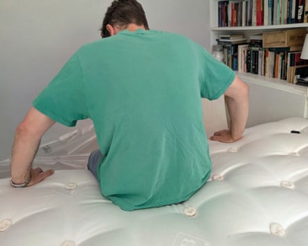 A man in a green T-shirt with his back to the camera sits on the edge of a Millbrook Wool Luxury 4000 Mattress