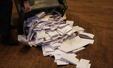 an official empties a wheelie bin full of ballot papers on to a parquet floor