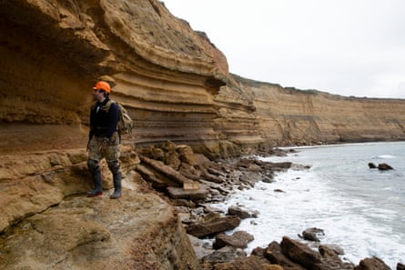 Man in orange hardhat walking at bottom of sea cliffs
